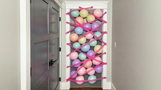 A doorway is filled with colorful pastel balloons held in place by a crisscross pattern of pink crepe paper streamers.