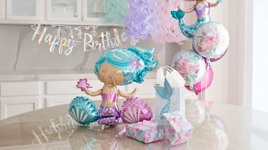 Mermaid birthday party decorations with pastel balloons, jellyfish lanterns, gift boxes, and “Happy Birthday” banner for an under-the-sea themed celebration.
