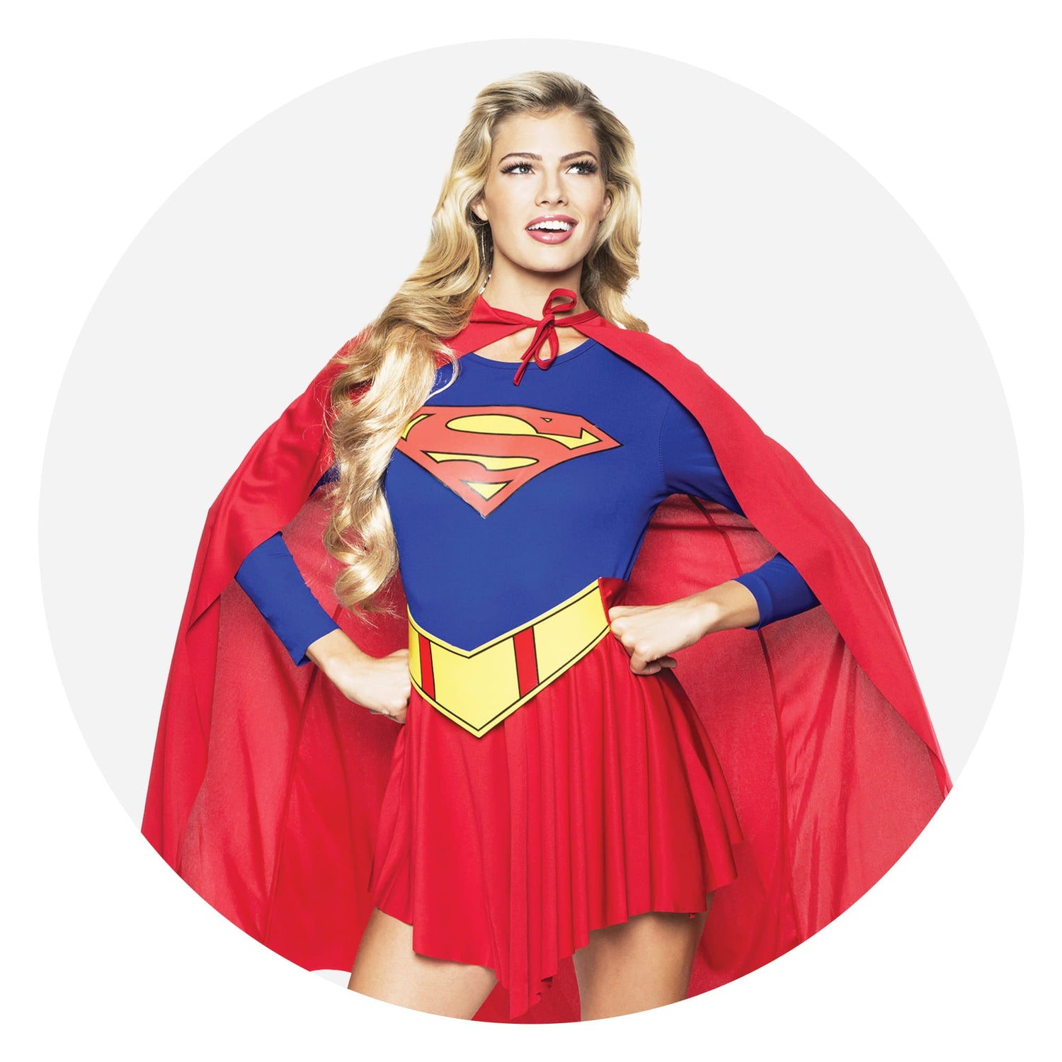 A woman wearing a Supergirl costume with a blue long-sleeved top, red skirt, red cape, and yellow belt posing against a white circular background.
