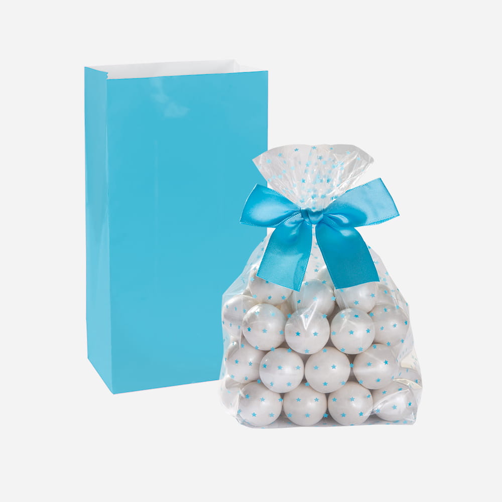 A blue paper party bag stands behind a clear cellophane bag filled with white gumballs and tied with a blue satin ribbon.