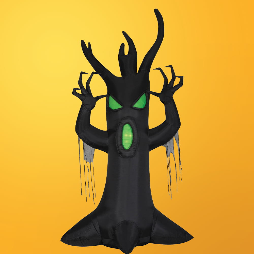 An inflatable black Halloween tree with glowing green eyes and mouth, claw-like branches, and tattered fabric hanging from its arms against a yellow background.